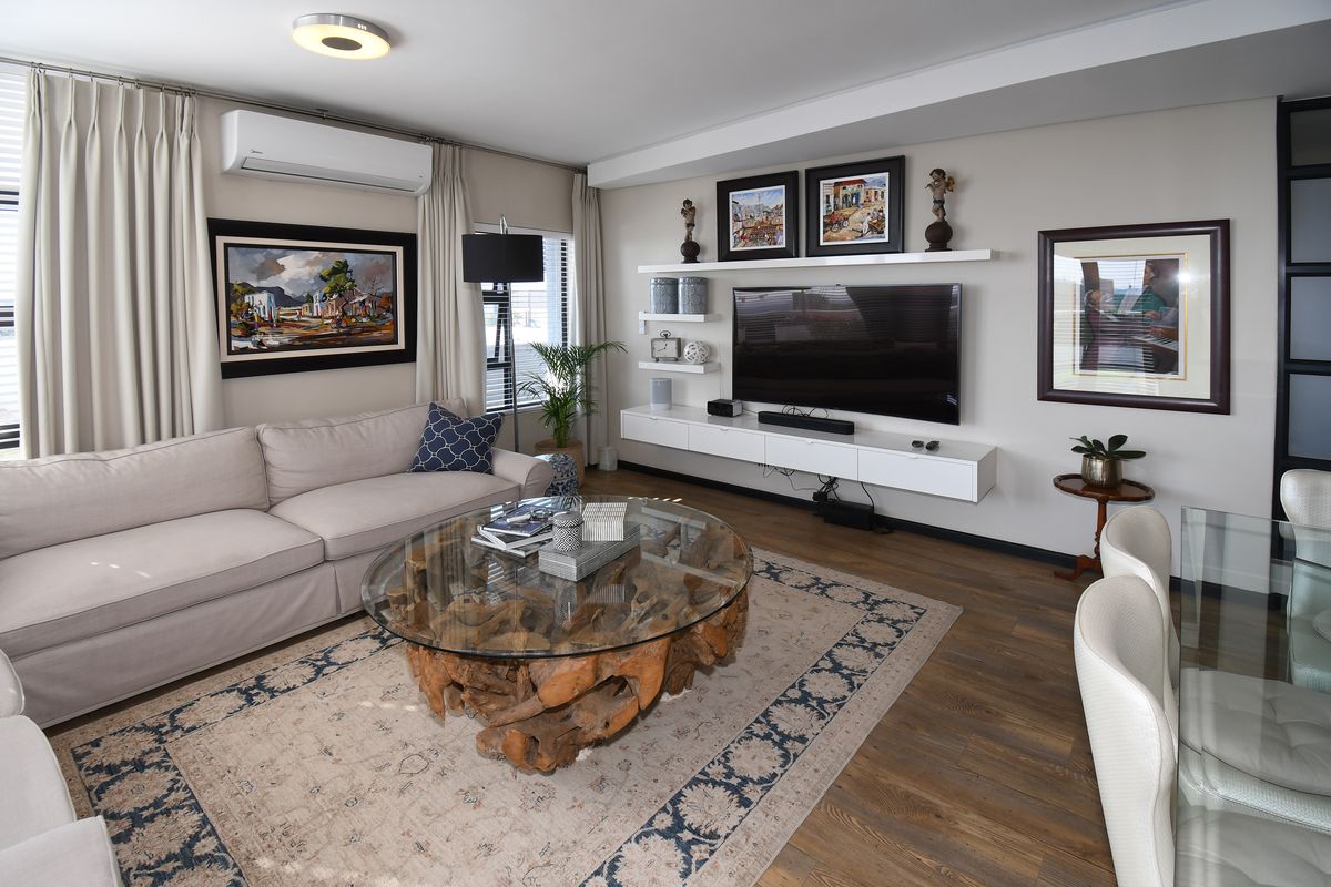 A well-maintained living room featuring modern floating cabinetry, wall-mounted shelving, air conditioning, and high-quality laminate flooring.