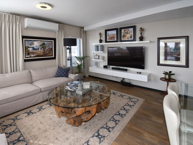 A well-maintained living room featuring modern floating cabinetry, wall-mounted shelving, air conditioning, and high-quality laminate flooring.