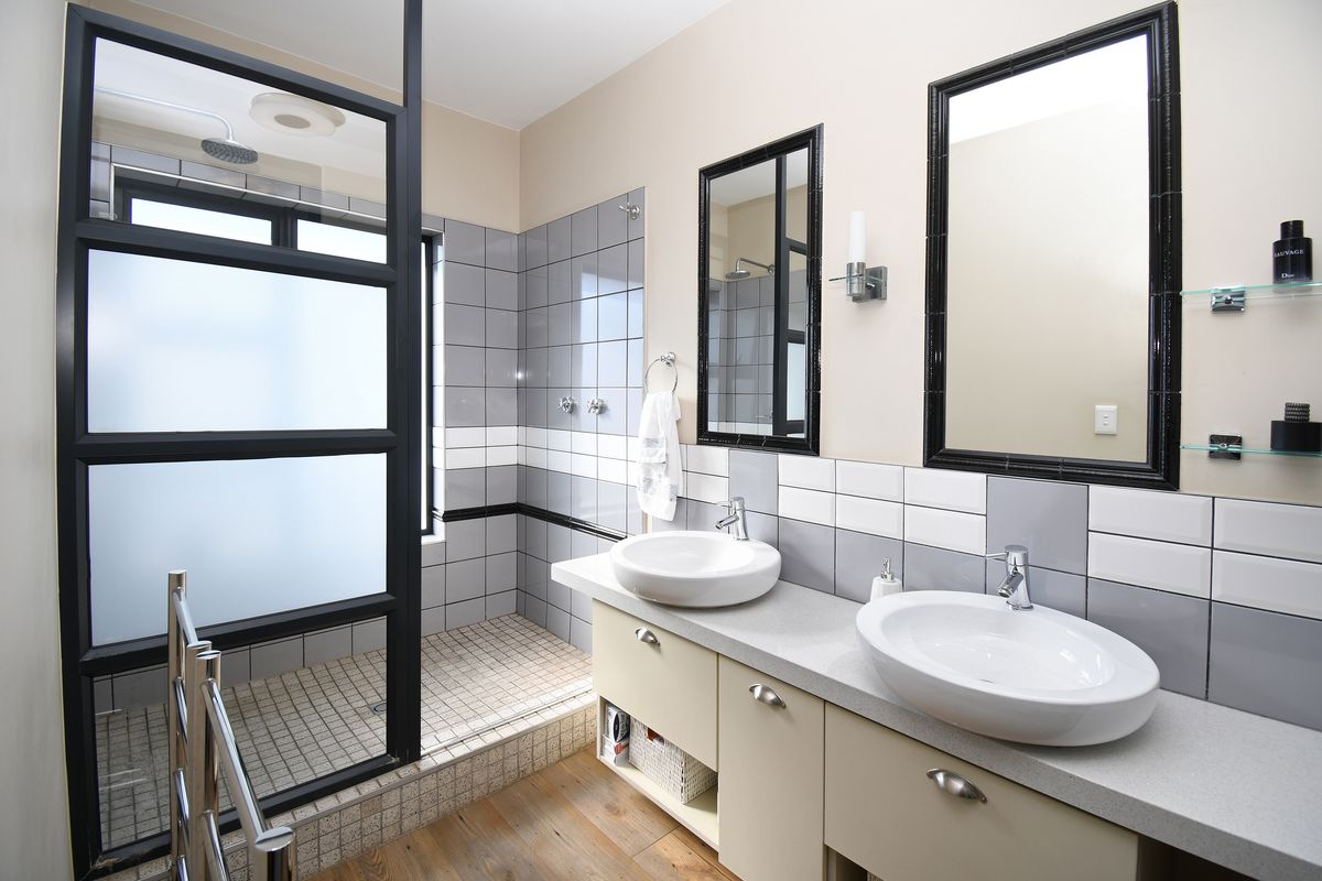 Modern bathroom featuring a double vanity with vessel sinks, a spacious walk-in shower with a frosted glass screen, and contemporary grey and white tiling.
