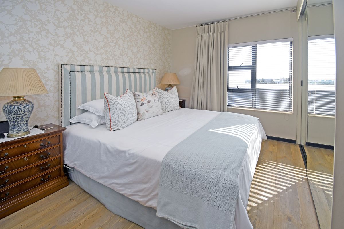 A well-maintained bedroom featuring timber flooring, a built-in wardrobe with mirrored doors, and large windows with venetian blinds allowing natural light.