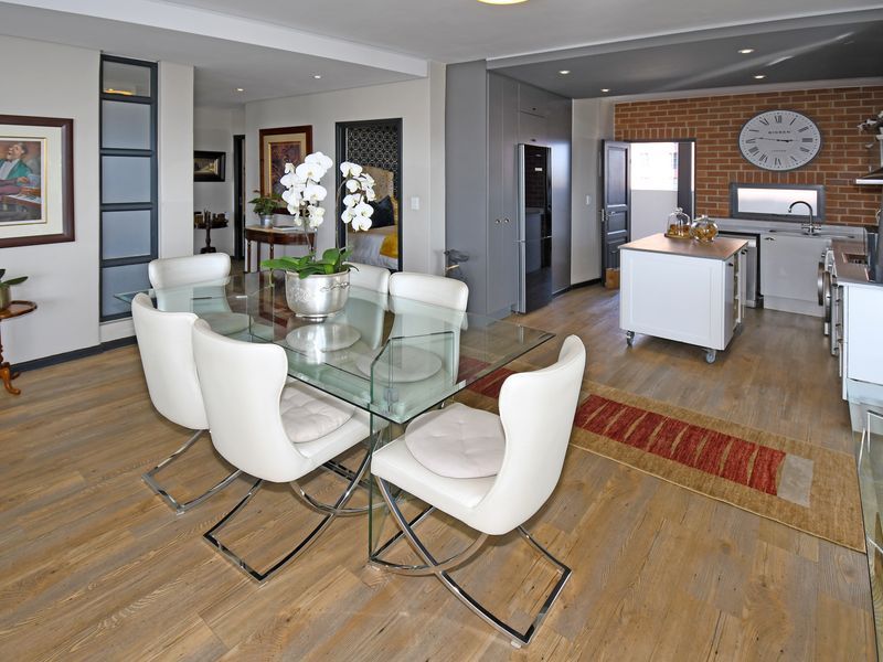 Spacious open-plan living and dining area featuring modern kitchen cabinetry, a central island, and stylish exposed brick accents with durable laminate flooring throughout.