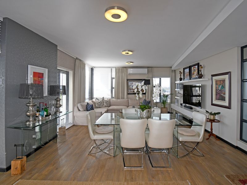 Spacious open-plan living and dining area featuring laminate flooring, modern ceiling lighting, wall-mounted air conditioning, and integrated shelving.