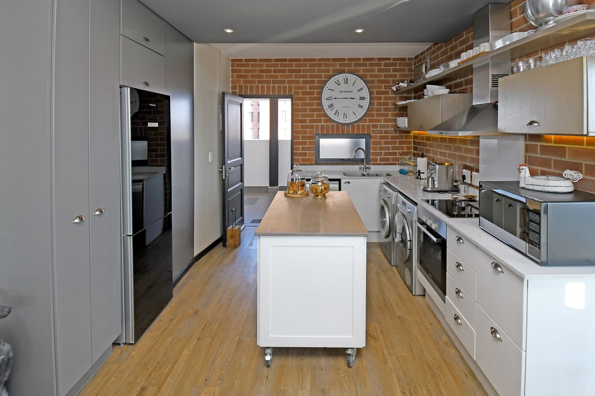 Modern kitchen featuring exposed brick walls, sleek cabinetry, integrated appliances, and a central island, offering a contemporary and functional culinary space.