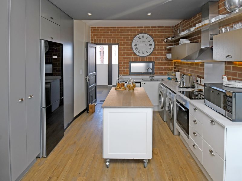 Modern kitchen featuring exposed brick walls, sleek cabinetry, integrated appliances, and a central island, offering a contemporary and functional culinary space.