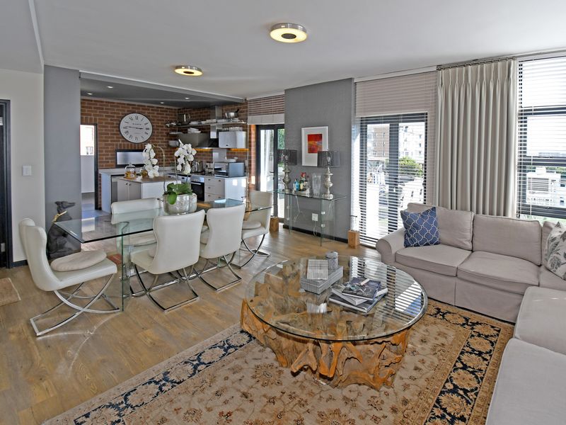 Spacious open-plan living and dining area featuring laminate flooring, exposed brick accents in the kitchen, and large sliding doors leading to a balcony.