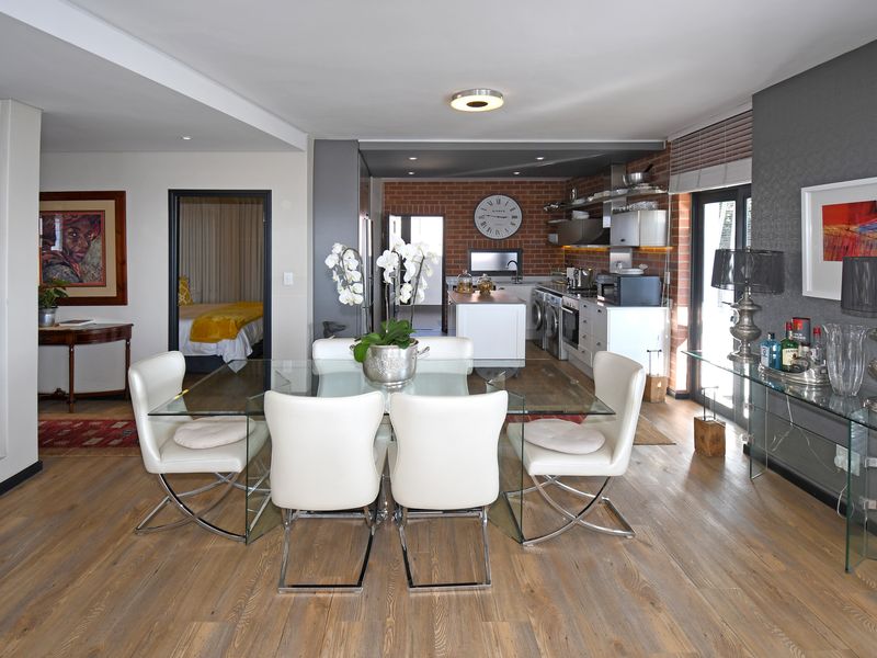 An open-plan living and dining area featuring hardwood floors, an exposed brick kitchen wall, and a central kitchen island with modern finishes.