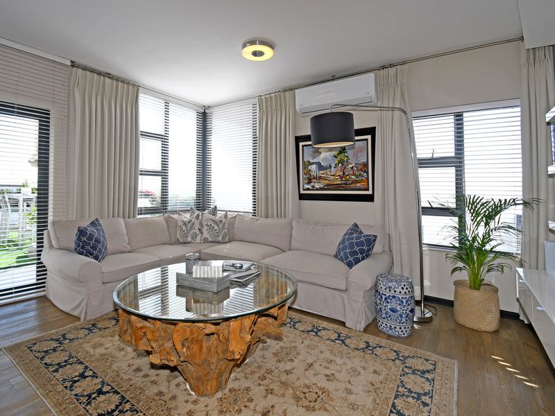 A bright and well-maintained living room featuring laminate flooring, split-system air conditioning, and large windows with integrated blinds and curtain tracks.