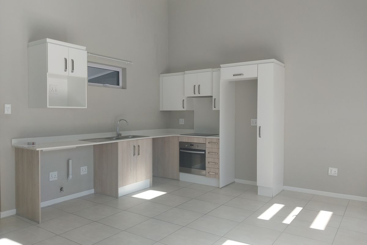 A clean, modern kitchen featuring built-in cabinetry, a stainless steel sink, and integrated oven and hob, set against neutral tiled flooring.