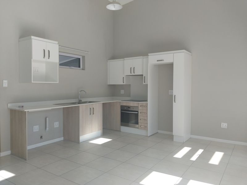 A clean, modern kitchen featuring built-in cabinetry, a stainless steel sink, and integrated oven and hob, set against neutral tiled flooring.