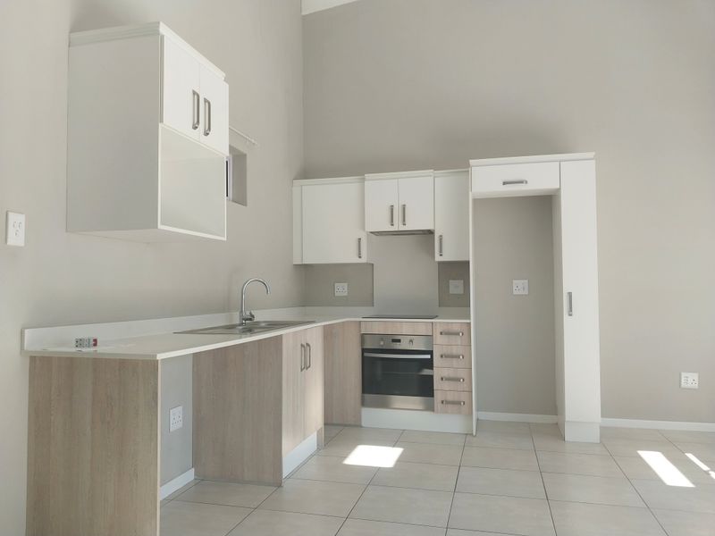Modern, clean-lined kitchen featuring light wood-tone cabinetry, white upper cabinets, integrated oven and hob, and neutral tiled flooring in an open-plan layout.