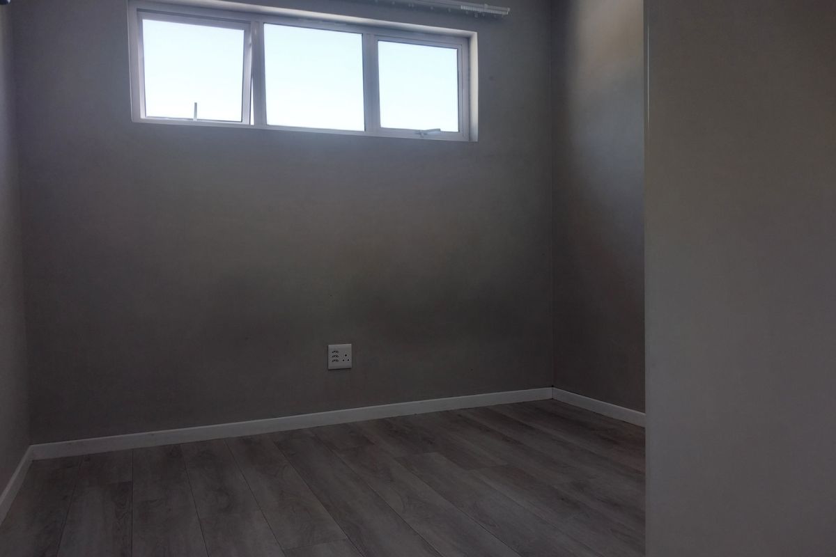 An empty bedroom featuring modern grey laminate flooring, neutral walls, and a window providing natural light.