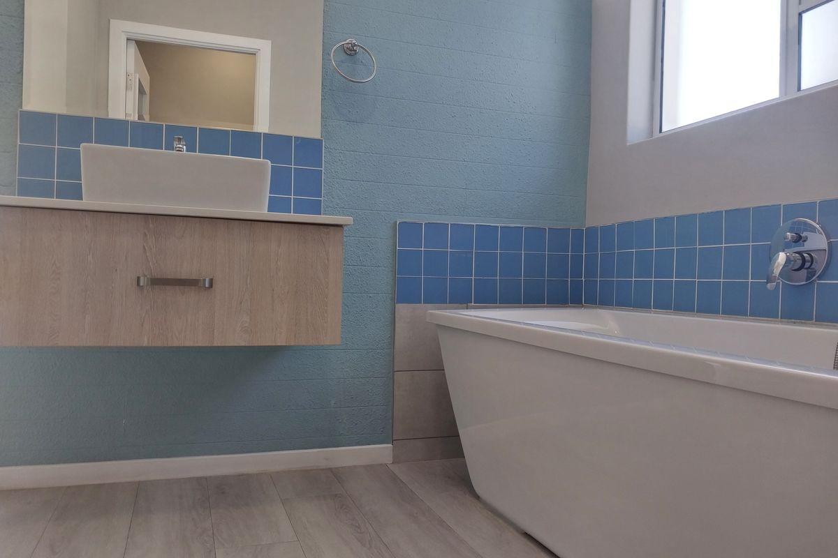 Modern bathroom featuring a floating vanity with vessel sink, a freestanding bathtub, and blue tiled accents.