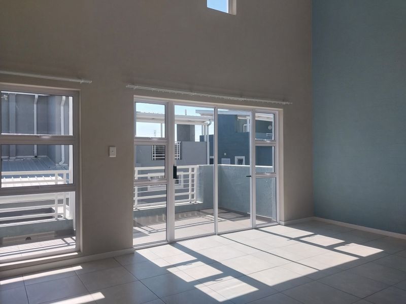Bright and spacious living area featuring double volume ceilings, tiled flooring, and large aluminium sliding doors leading to an outdoor balcony.