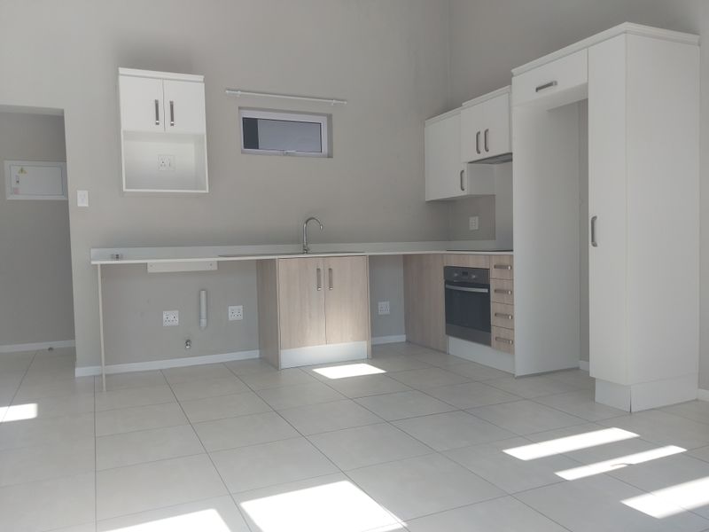A clean, modern, and empty kitchen featuring light-toned cabinetry, built-in oven, tiled flooring, and ample counter space in a neutral color palette.