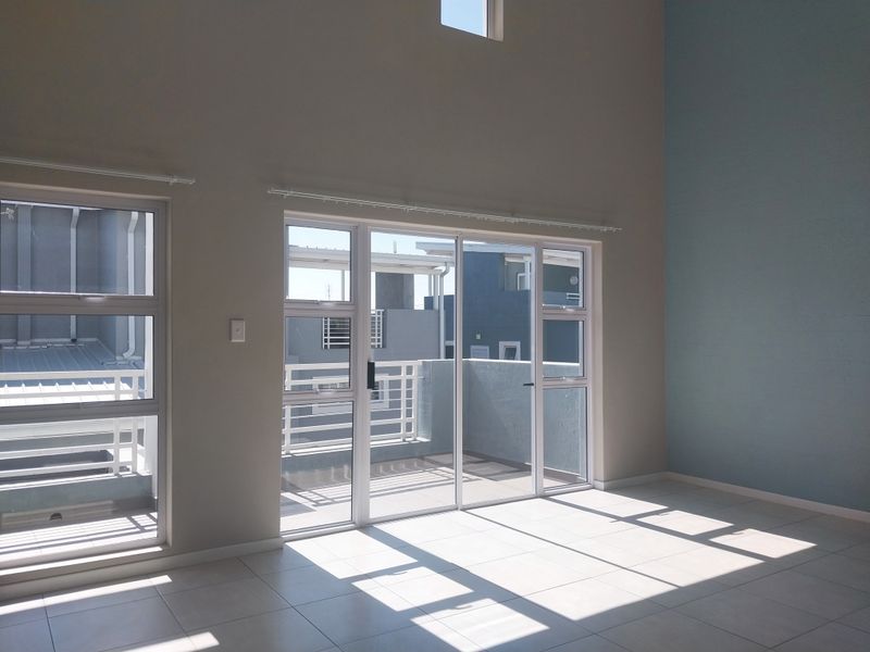 Bright and spacious living area featuring high ceilings, tiled flooring, and large aluminium sliding doors leading to an outdoor balcony.