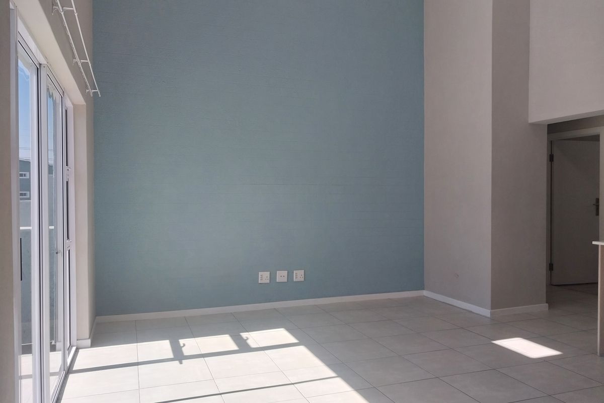 A bright, empty living area featuring high ceilings, neutral tiled flooring, and a large sliding glass door providing ample natural light.
