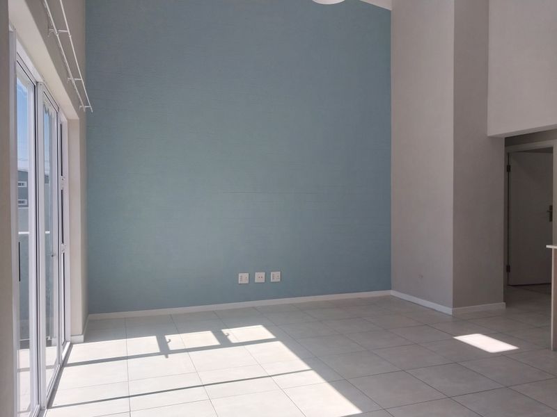 A bright, empty living area featuring high ceilings, neutral tiled flooring, and a large sliding glass door providing ample natural light.