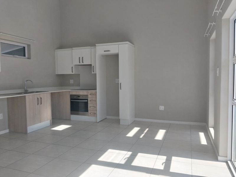 Bright open-plan kitchen and living area featuring modern cabinetry, built-in oven, hob, and neutral tiled flooring, offering a clean and versatile living space.