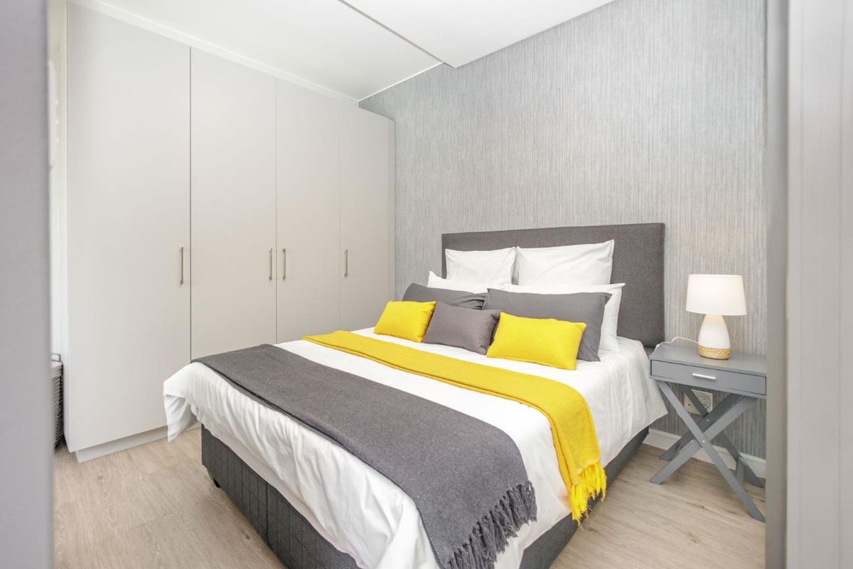 A well-maintained bedroom featuring light laminate flooring, neutral textured wallpaper, and ample built-in cupboard storage.
