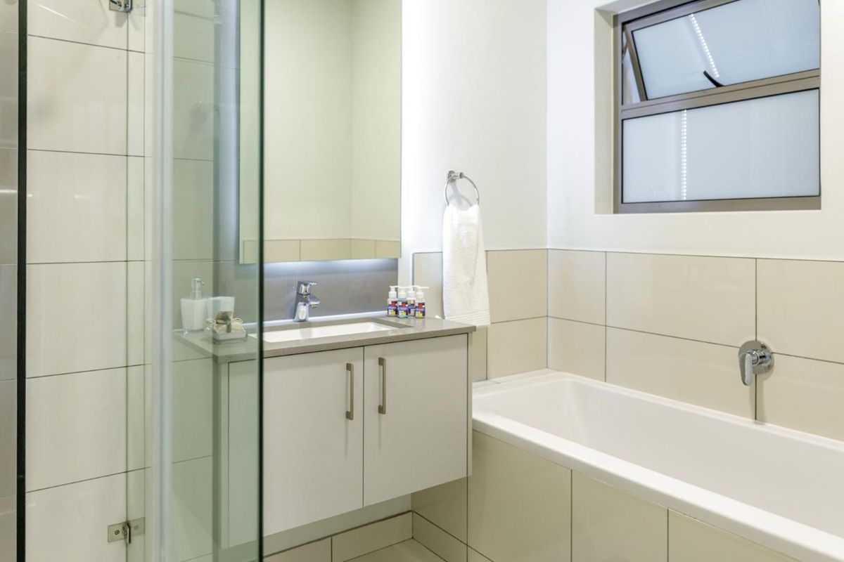 Modern bathroom featuring a vanity with basin, a bathtub, and a separate glass-enclosed shower with neutral wall and floor tiling.