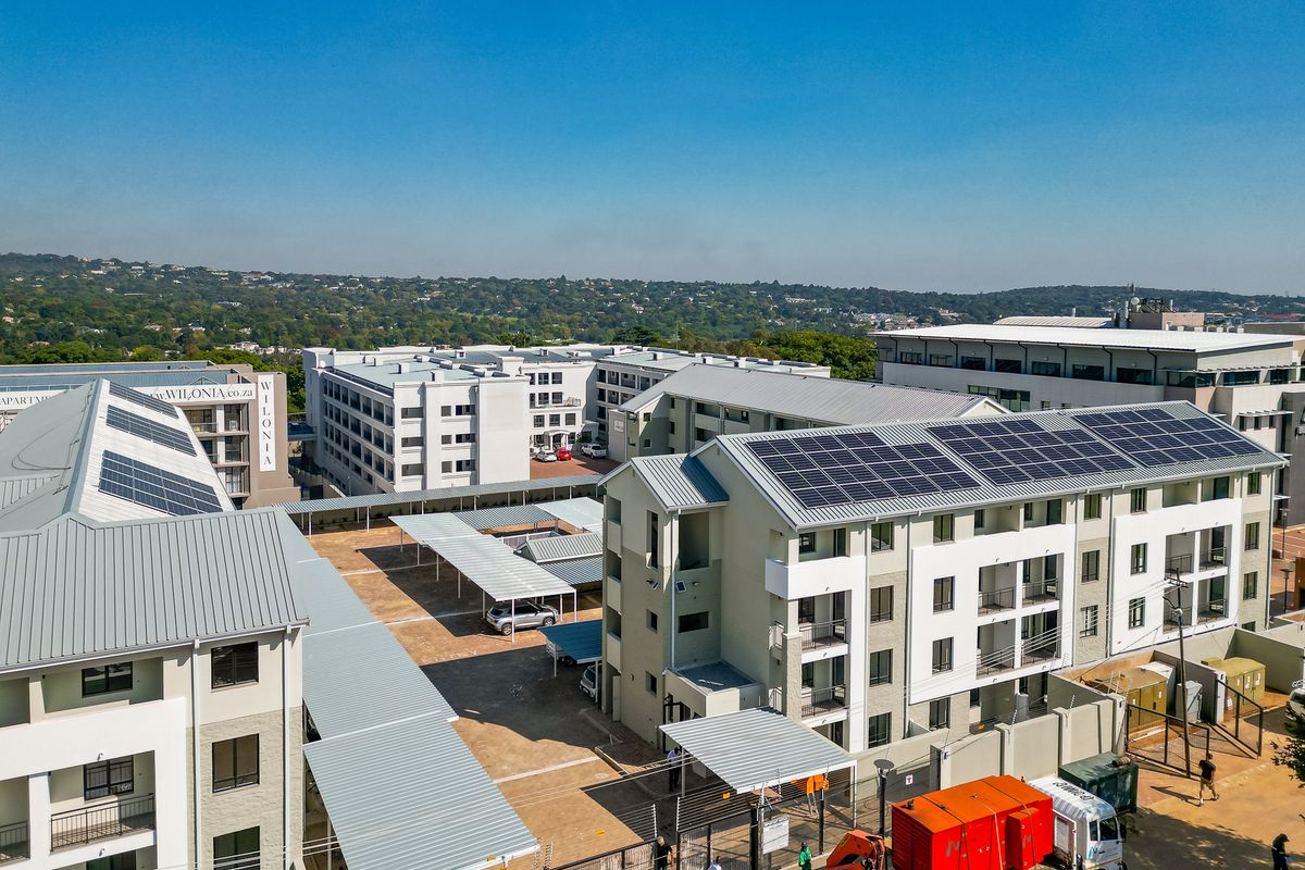 Aerial view of a modern apartment complex featuring multiple residential blocks, covered parking bays, and rooftop solar panel installations.