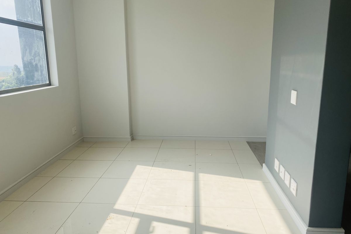 A bright, empty room featuring neutral wall tones, large windows, and tiled flooring, suitable for use as a bedroom or home office.
