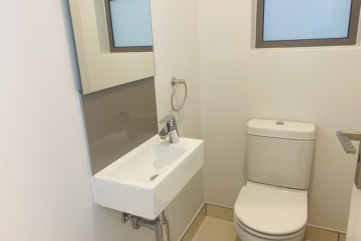 A compact guest bathroom featuring a wall-mounted basin, modern chrome tapware, a toilet, and a mirror with a neutral splashback.