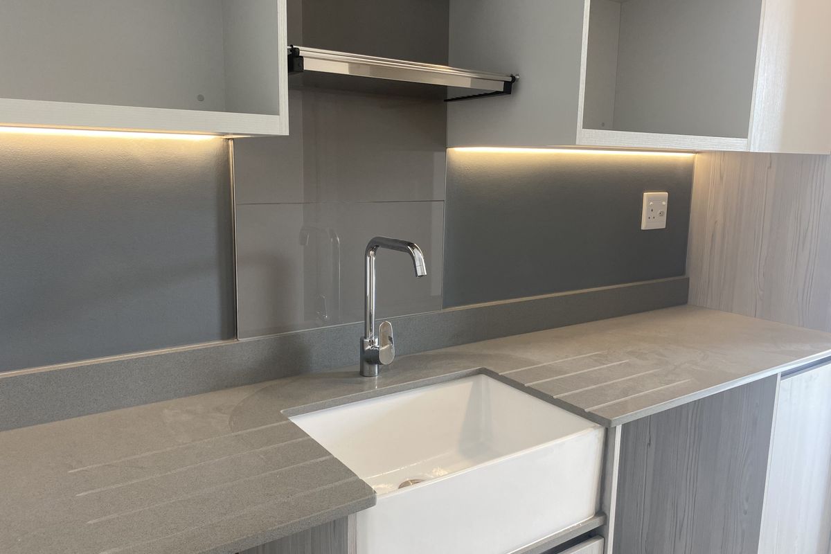 Modern kitchen area featuring a farmhouse-style sink, stone countertops, integrated cabinetry, and under-cabinet LED lighting.
