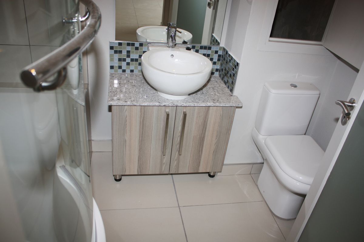 A modern bathroom featuring a vessel sink on a granite vanity, mosaic tile backsplash, toilet, and a glass shower enclosure.