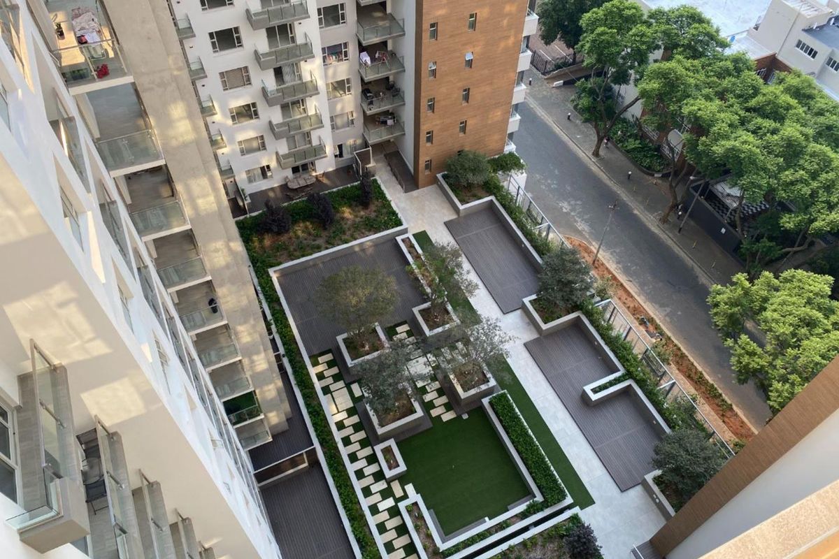An elevated aerial view of a modern apartment complex featuring a well-maintained landscaped courtyard with timber decking, raised garden beds, and paved walkways.