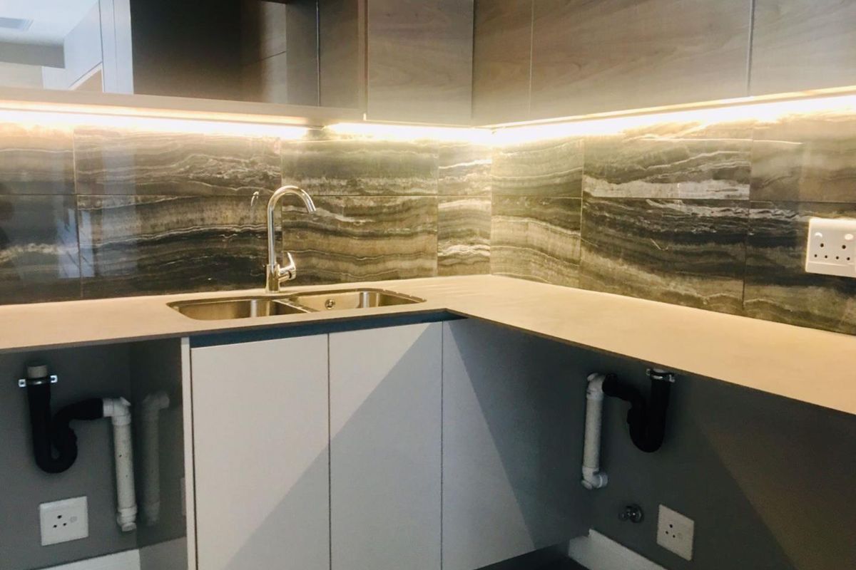 Modern kitchen area featuring stone-look backsplash, under-cabinet lighting, and built-in cabinetry with an undermount double sink.
