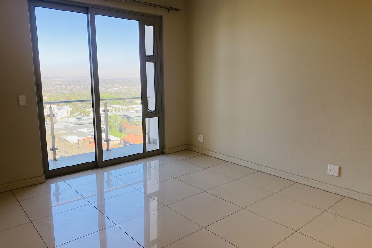 A bright, empty bedroom featuring large sliding glass doors that open to a balcony with expansive elevated views and polished floor tiles.