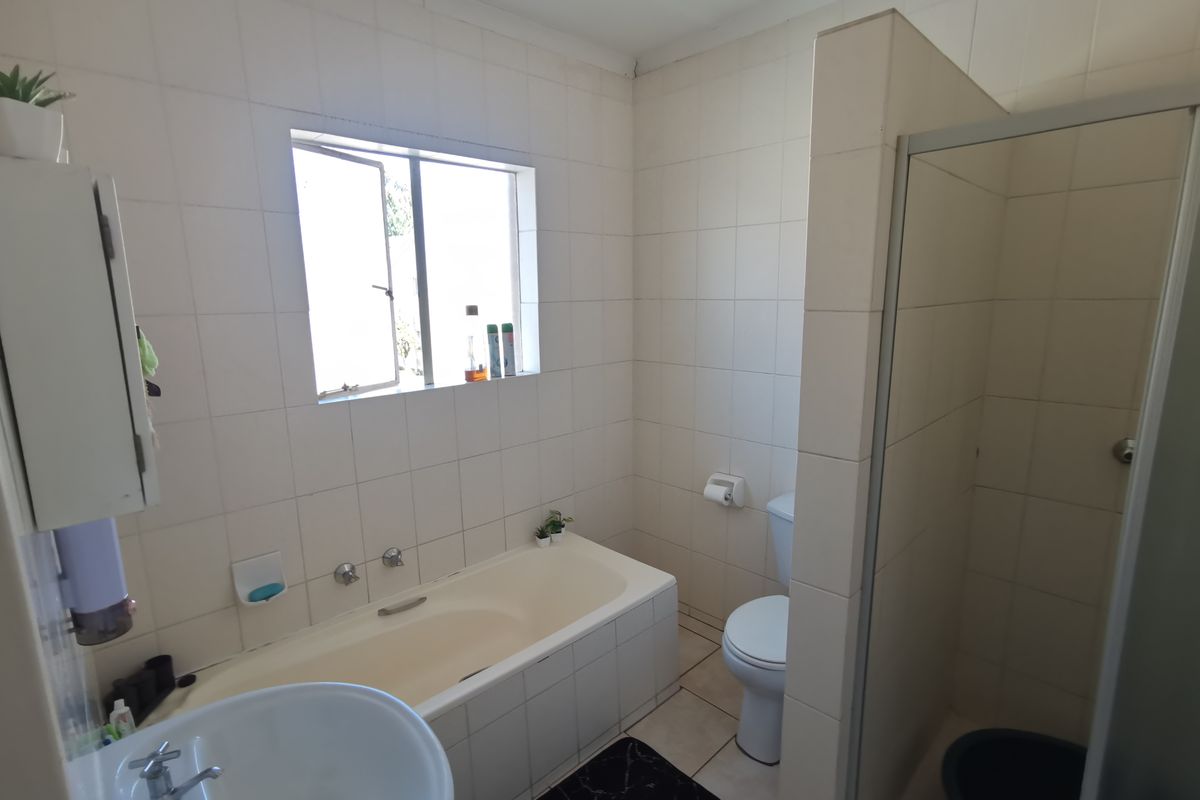 A functional bathroom featuring a built-in bathtub, separate shower enclosure, toilet, and pedestal basin with neutral wall tiling.