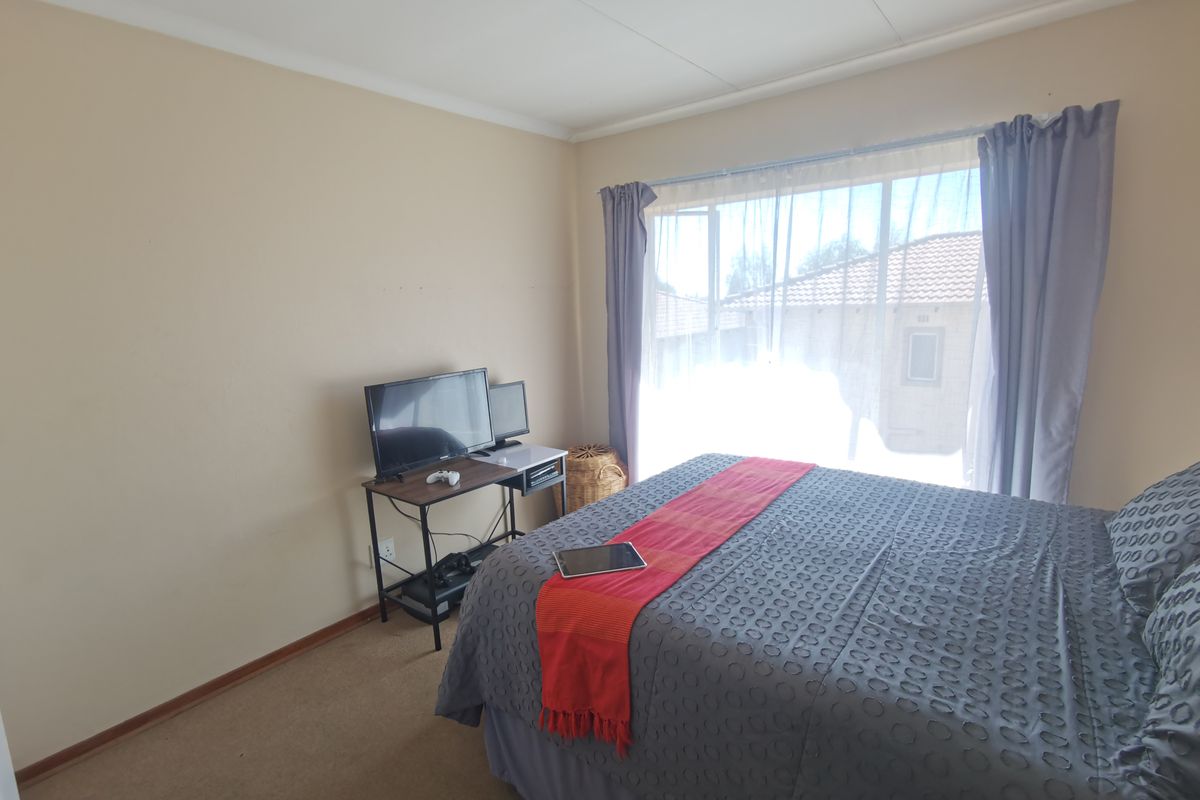 A bedroom featuring carpeted flooring and a large window with curtains, providing natural light and a view of the exterior.