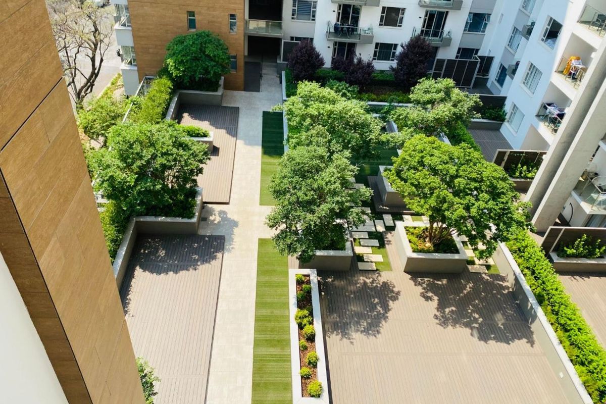 An elevated aerial view of a well-maintained apartment complex courtyard featuring landscaped gardens, raised planters, and modern composite decking areas.