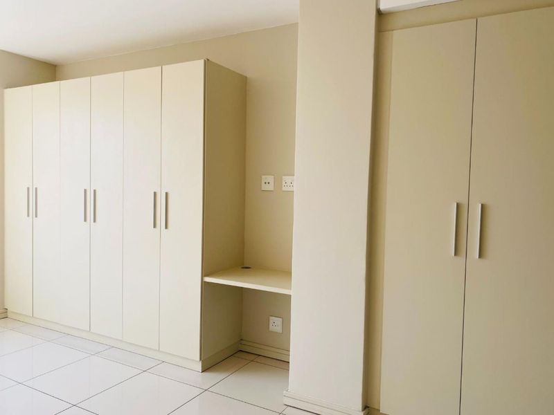 A clean, modern bedroom featuring extensive built-in cabinetry with an integrated desk area and neutral tiled flooring.