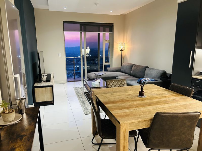 Modern open-plan living and dining area featuring sleek tiled floors, recessed lighting, and direct access to a balcony with sunset views.