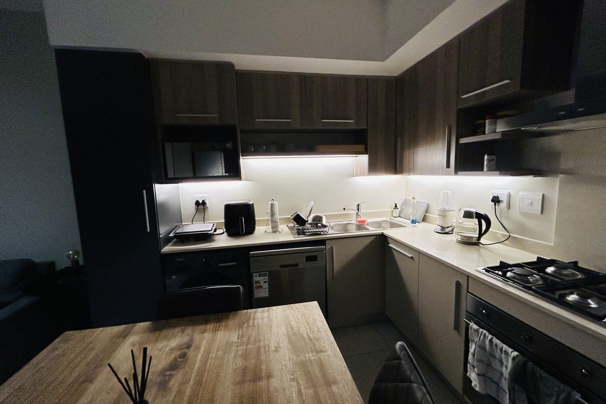 Modern kitchen featuring dark wood cabinetry, stone countertops, integrated appliances, gas hob, and under-cabinet lighting.