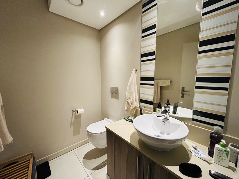 A modern bathroom featuring a wall-mounted toilet, a sleek vanity cabinet with a vessel sink, and a large decorative mirror.