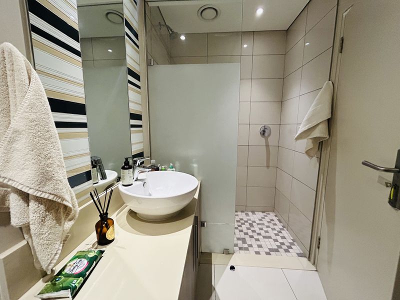 Modern bathroom featuring a vessel sink on a vanity cabinet, a walk-in shower with a frosted glass screen, and contemporary wall tiling.