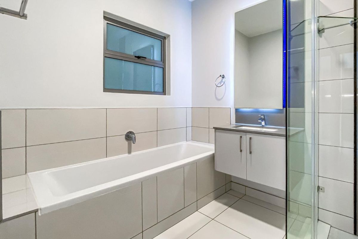 Modern bathroom featuring a built-in bathtub, wall-mounted vanity with integrated basin, and a glass-enclosed shower with neutral tiled finishes.