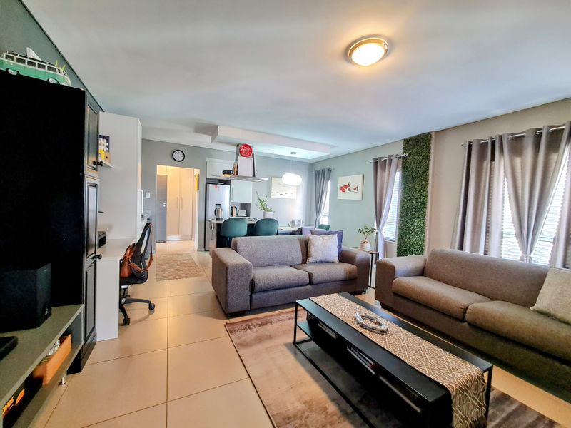 Open-plan living area featuring tiled flooring, a modern kitchen with breakfast bar, and integrated lighting, creating a functional and cohesive living space.