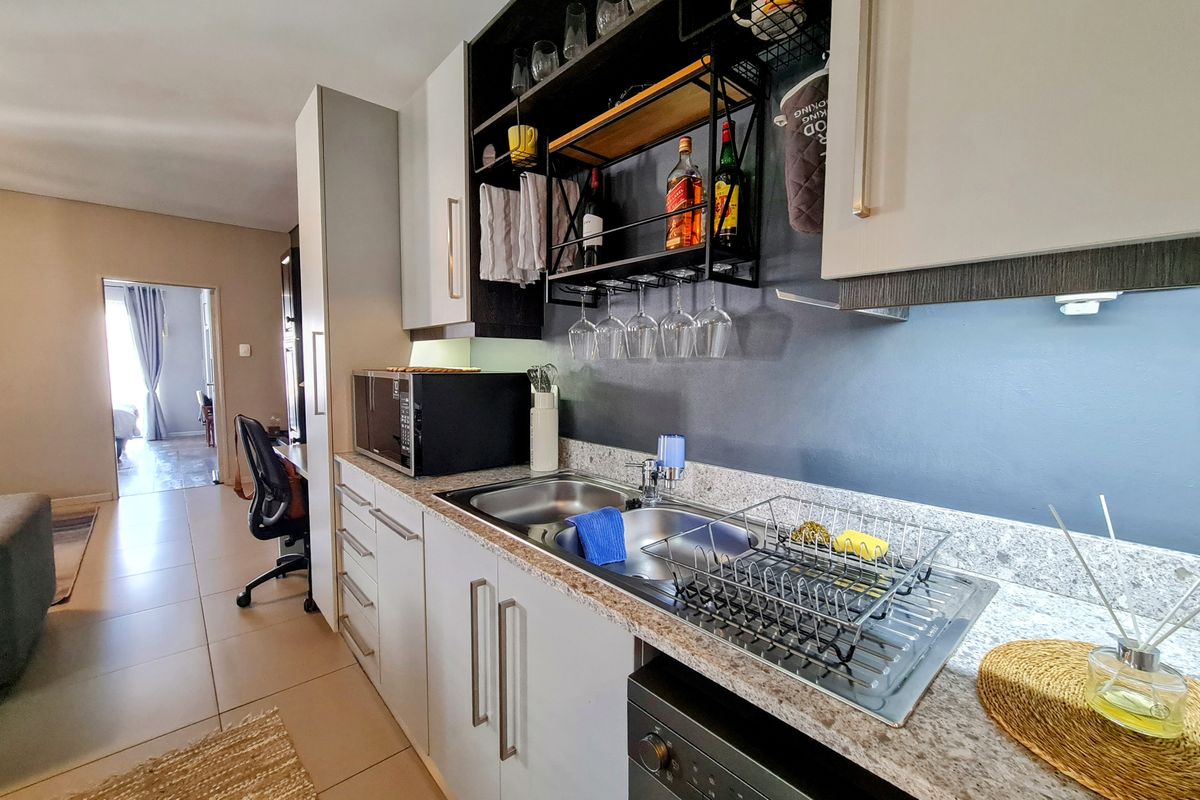 Modern kitchen featuring granite countertops, stainless steel double sink, integrated cabinetry, and under-cabinet lighting, seamlessly flowing into the adjacent living area.
