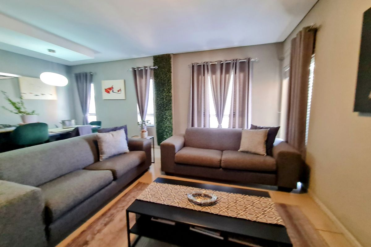 A comfortable living room featuring neutral wall tones, recessed ceiling lighting, and large windows with curtains, creating a bright and inviting atmosphere.