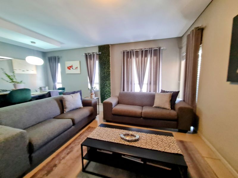 A comfortable living room featuring neutral wall tones, recessed ceiling lighting, and large windows with curtains, creating a bright and inviting atmosphere.