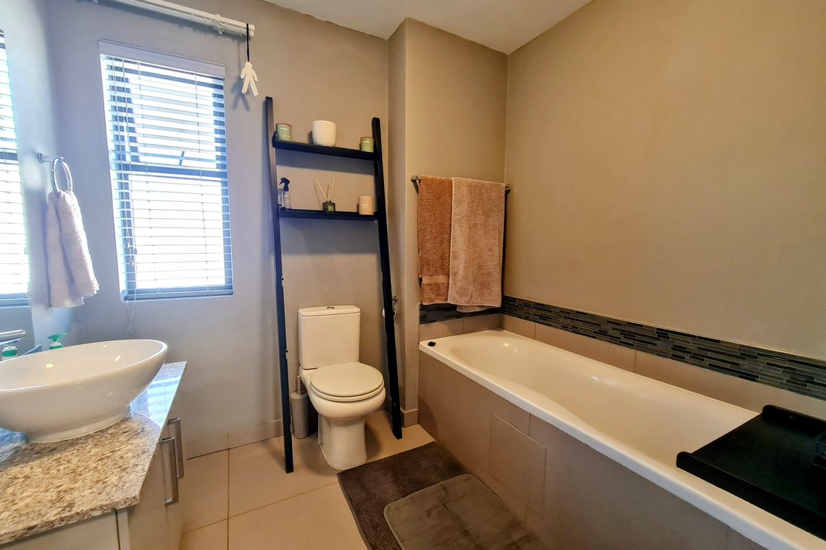 A functional bathroom featuring a built-in bathtub with mosaic tile accents, a modern vessel sink on a stone vanity, and a standard toilet.