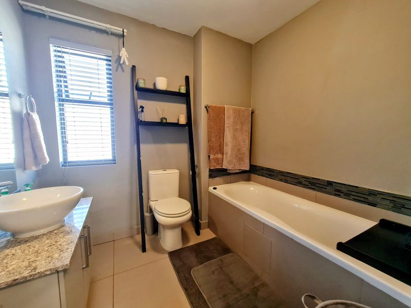 A functional bathroom featuring a built-in bathtub with mosaic tile accents, a modern vessel sink on a stone vanity, and a standard toilet.