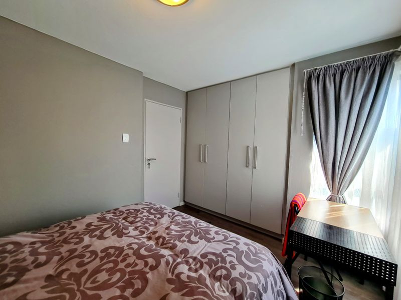A well-maintained bedroom featuring neutral wall tones, built-in floor-to-ceiling wardrobes, and natural light from the adjacent window.