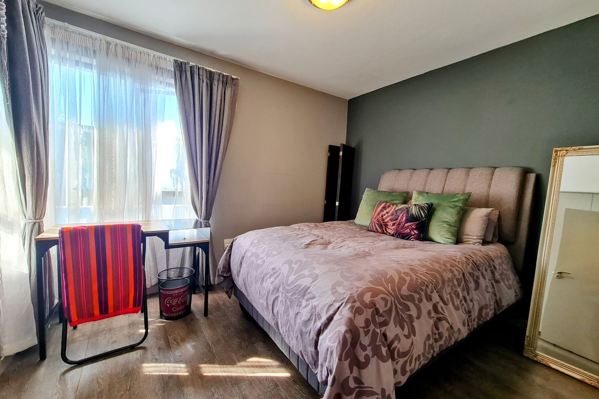 A bedroom featuring wood-look flooring, a dark accent wall, and a large window with curtain treatments.