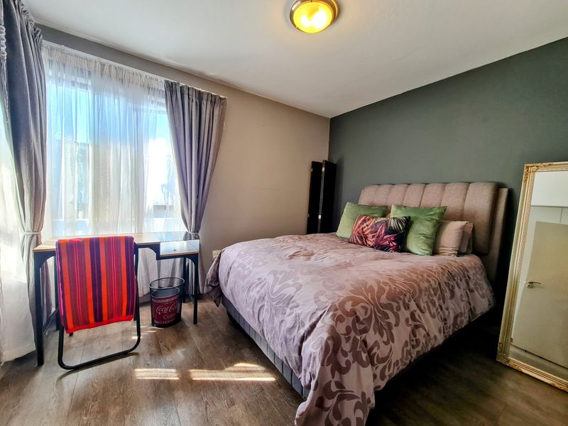 A bedroom featuring wood-look flooring, a dark accent wall, and a large window with curtain treatments.